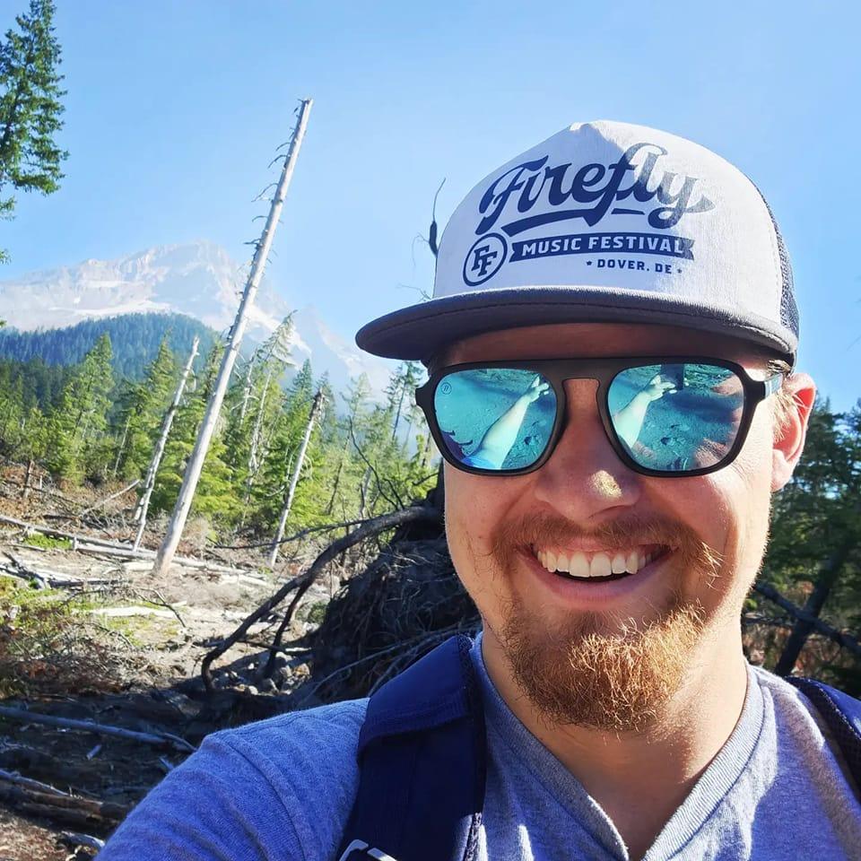 Owner and Founder standing in front of Mt. Hood, wearing a Firefly Music Festival hat